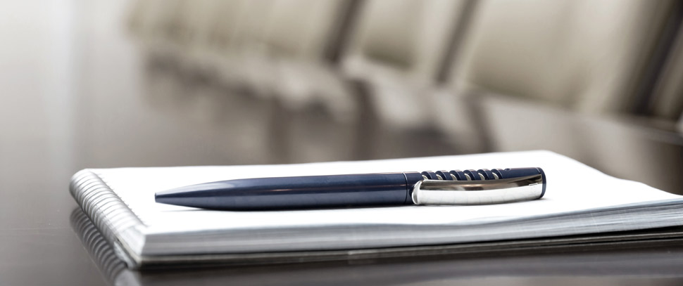 Pen sitting on long board desk with seats in background.